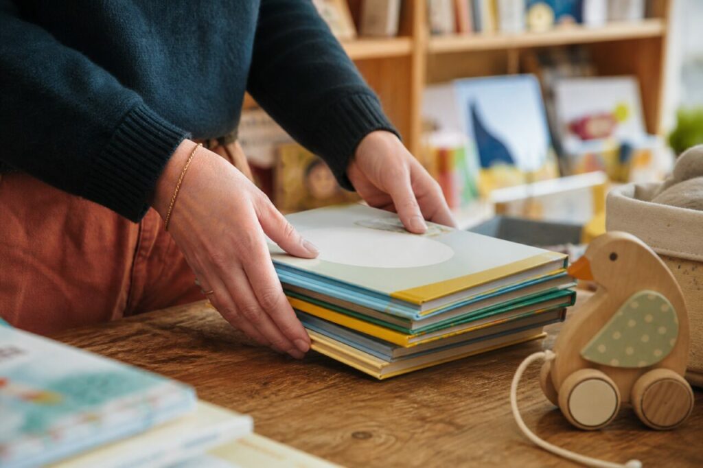 Album ouvert de librairie jeunesse près d’un jouet en bois et de petites mains
