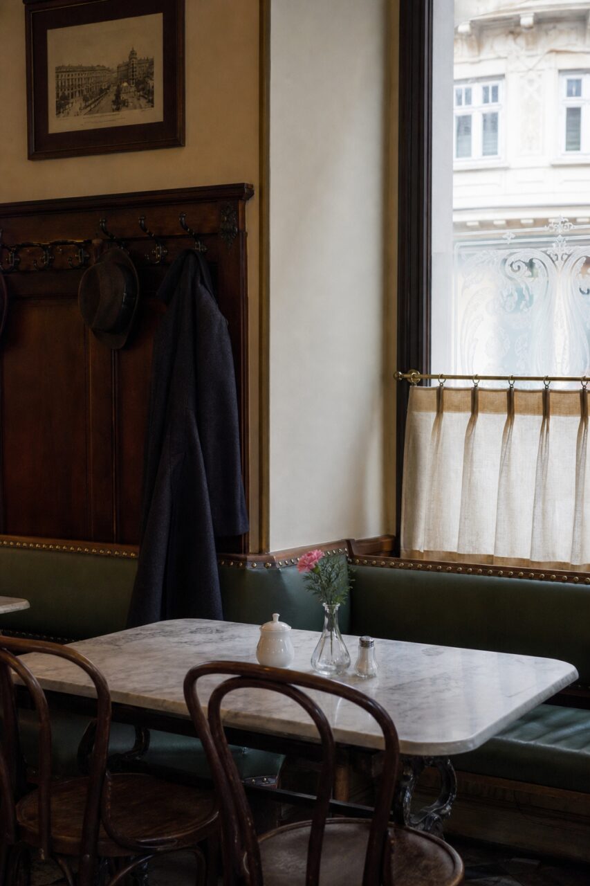 Banco verde oscuro, mesa clara y percheros junto a una ventana
