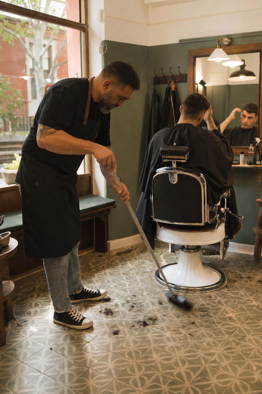 Barbier balayant les cheveux coupés autour d’un fauteuil de salon