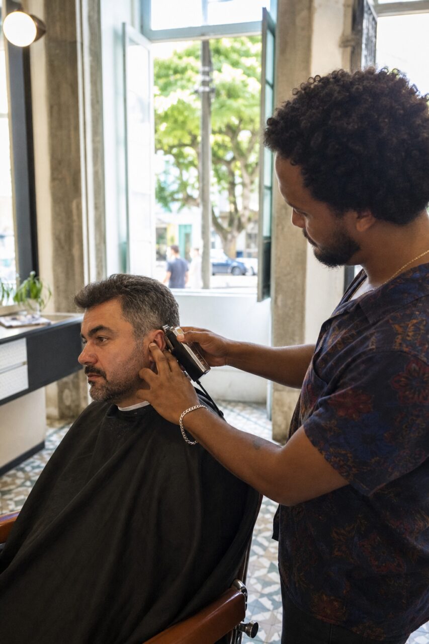 Barbiere rifinisce la basetta del cliente con il regolabarba vicino alla finestra aperta