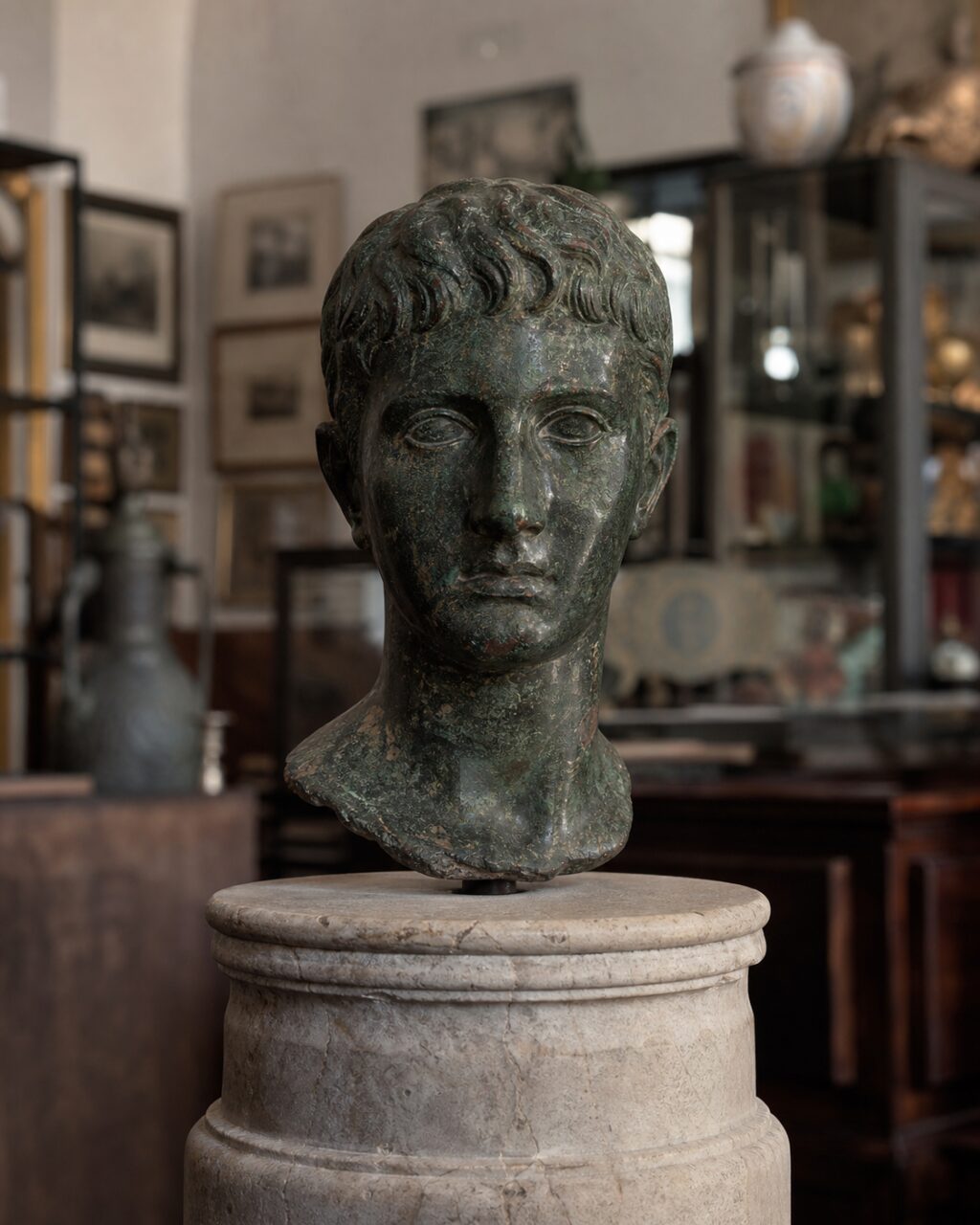 Frontal dark metal bust on a round stone pedestal
