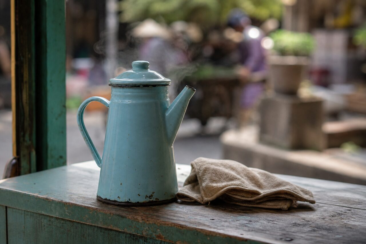 Cafeteira esmaltada e pano diante de uma rua desfocada