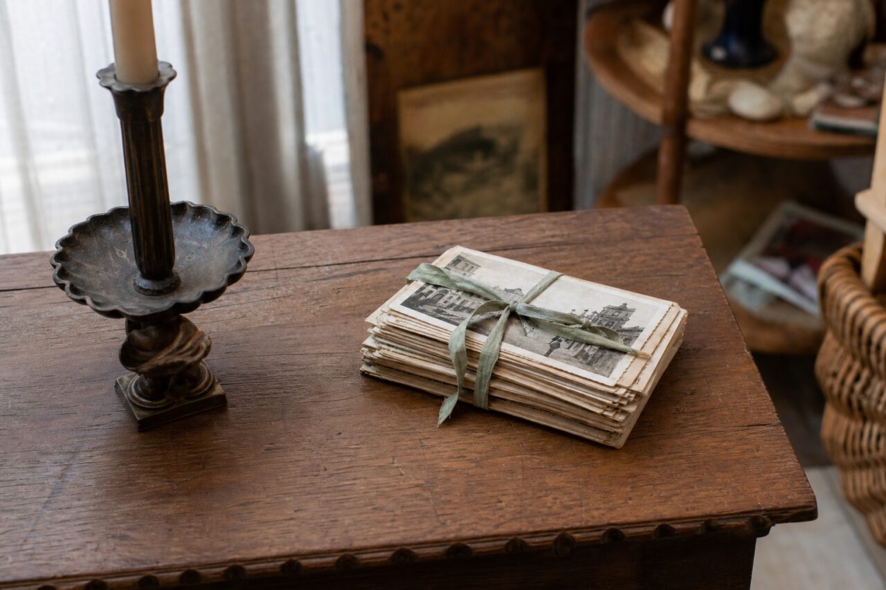Old postcards on a wooden table beside a dark candlestick
