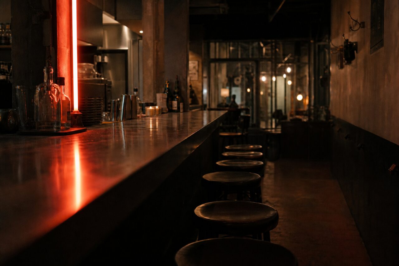 Balcão de bar escuro iluminado por tubo de néon vermelho e luzes quentes