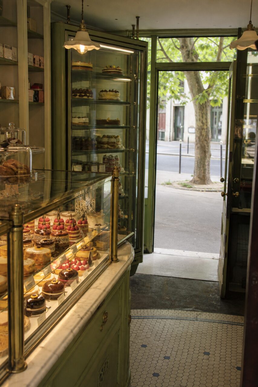 Mostrador verde de pastelería frente a una puerta abierta y un árbol