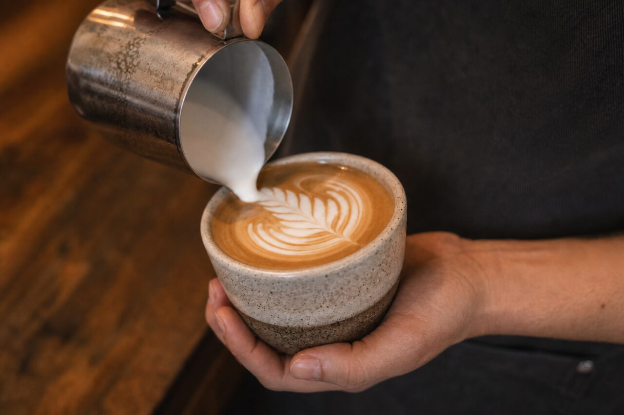 Close detail of a leaf pattern drawn in a coffee cup with a milk pitcher