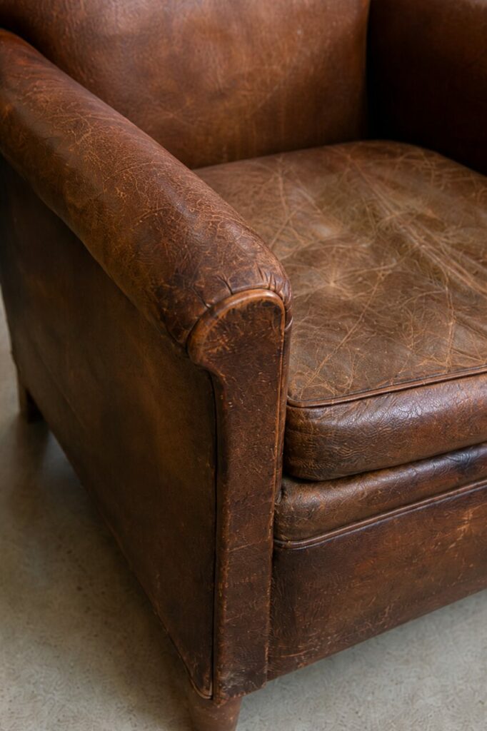 Détail vertical du fauteuil club en cuir brun patiné et de son coussin froissé