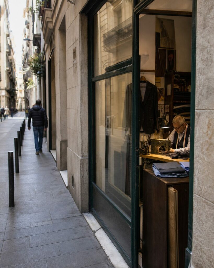Entrée vitrée d’une petite sastrería de Barcelone avec tailleur visible au travail
