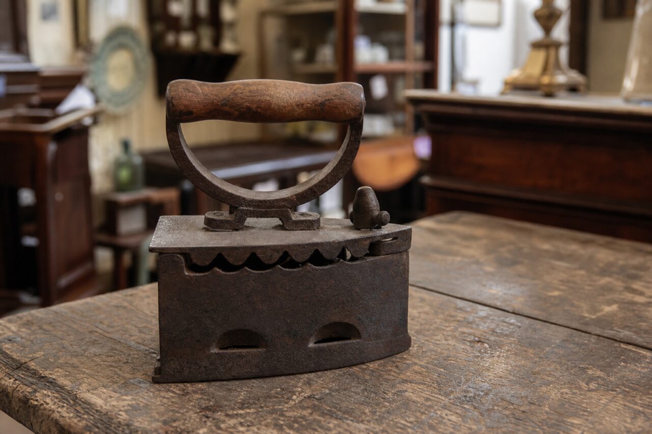 Oud gietijzeren strijkijzer met houten handvat op een tafel in een antiekwinkel