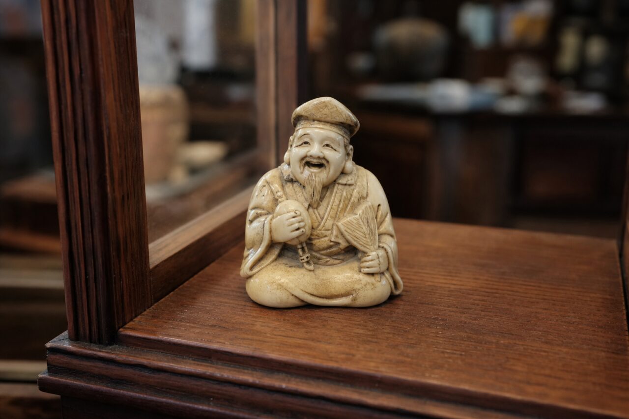 Figura de homem sentado e sorridente com leque