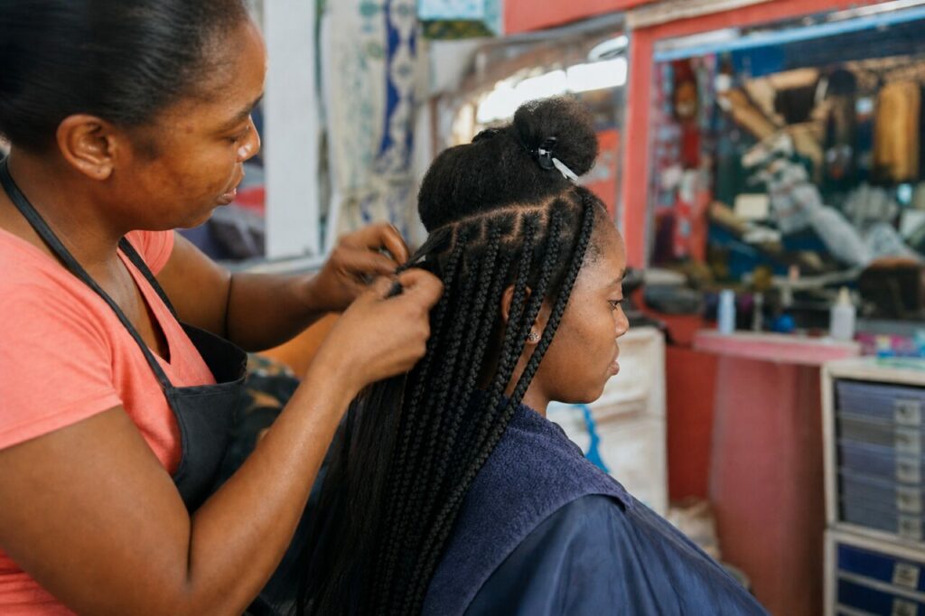 Mãos hábeis formam tranças pretas no salão