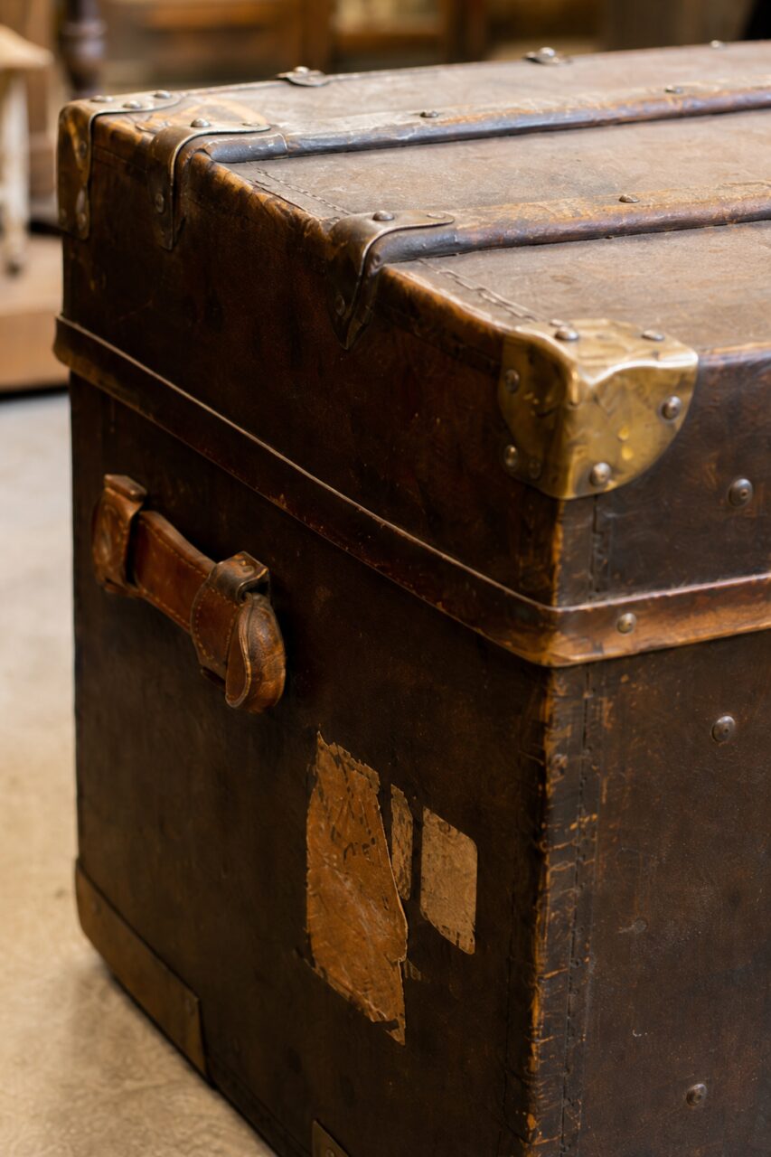 Close-up of the worn brown leather, side handle and metal corner guard on an old trunk