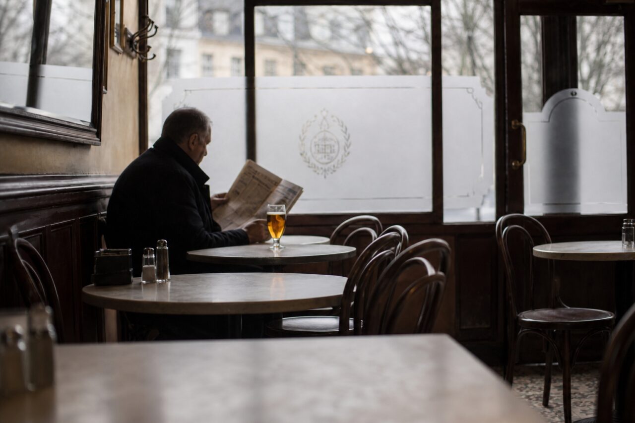 Newspaper reader and amber drink among round tables