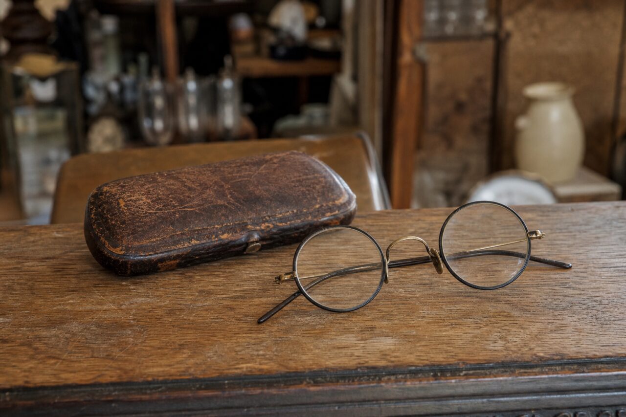Old round glasses and a worn leather case on a wooden table