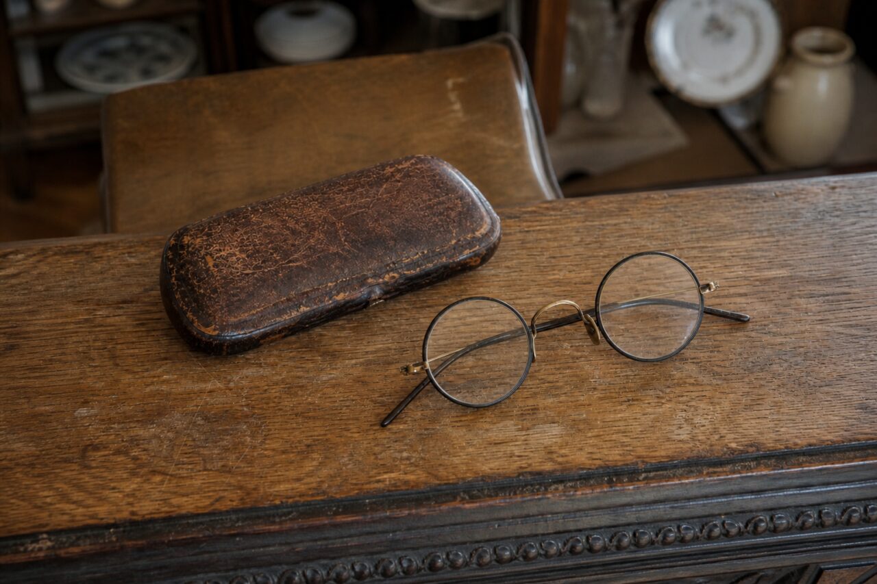 Ronde bril en bruin etui van iets bovenaf op een oude tafel