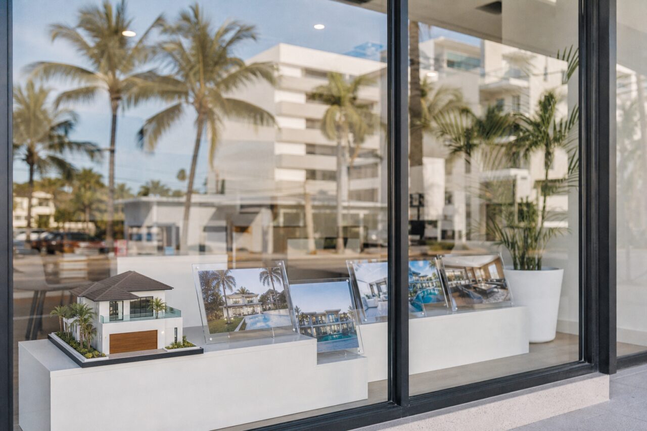 Maqueta de villa y fotografías de propiedades en un escaparate tropical
