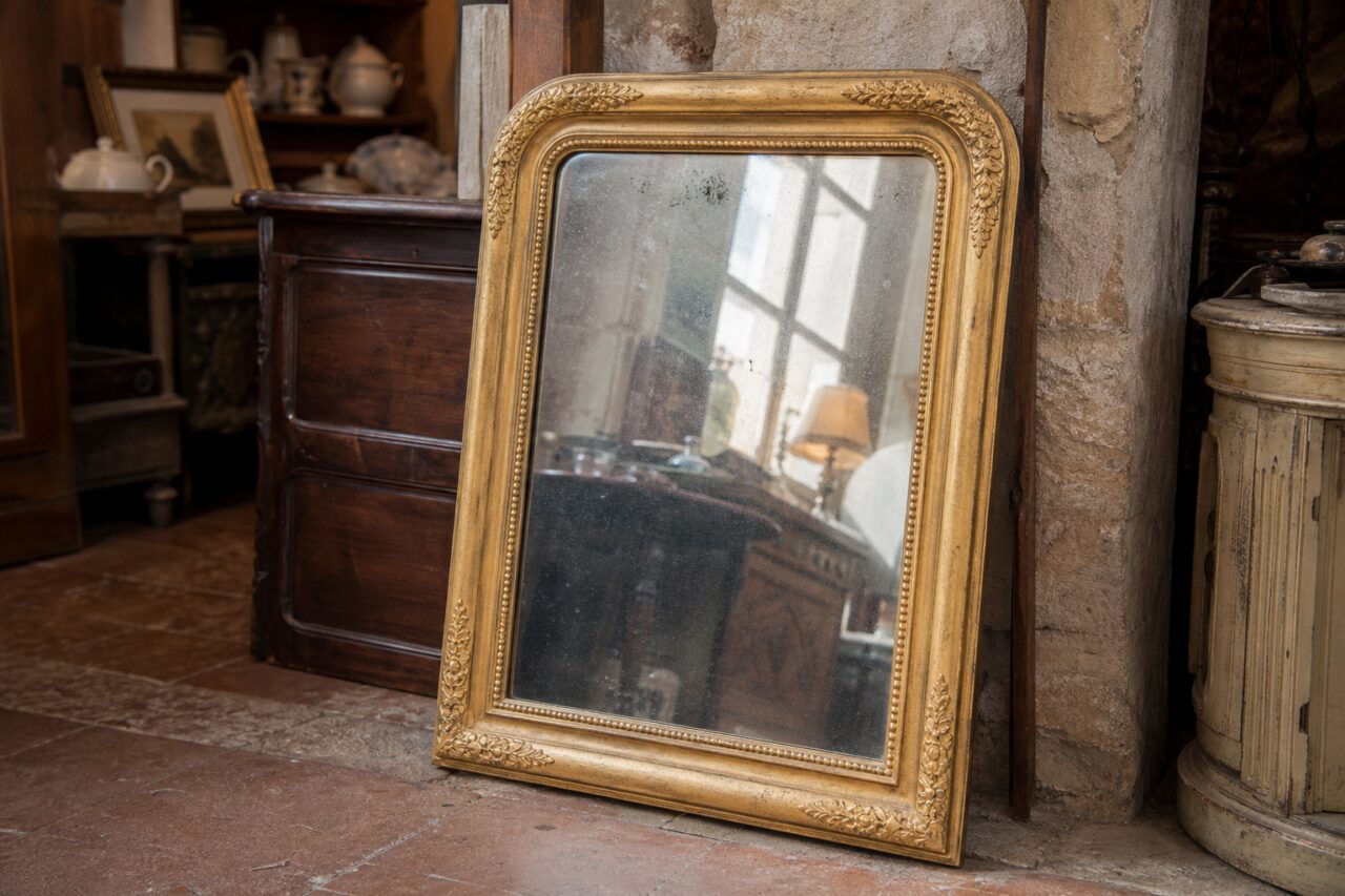 Miroir doré de style Louis-Philippe posé au sol dans une boutique d’antiquités