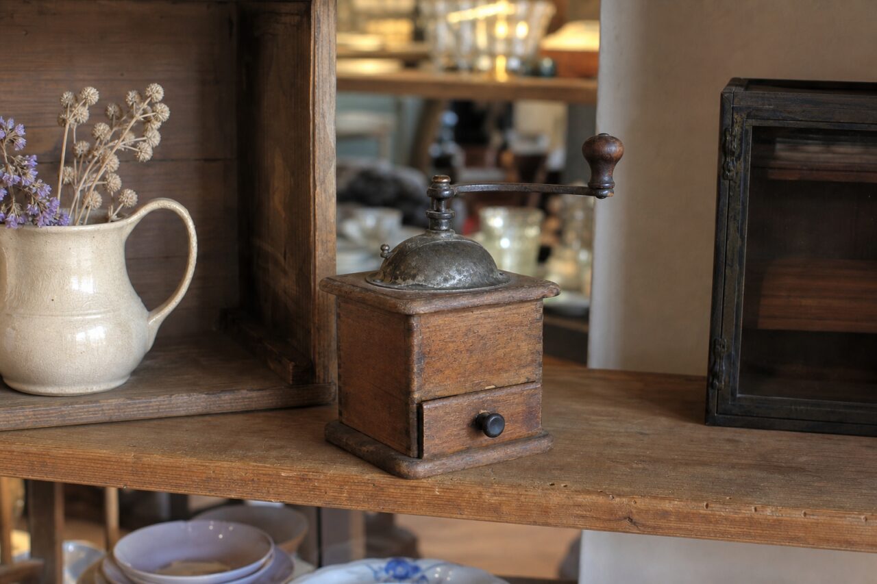 Macinacaffè antico in legno tra oggetti su uno scaffale d’antiquariato