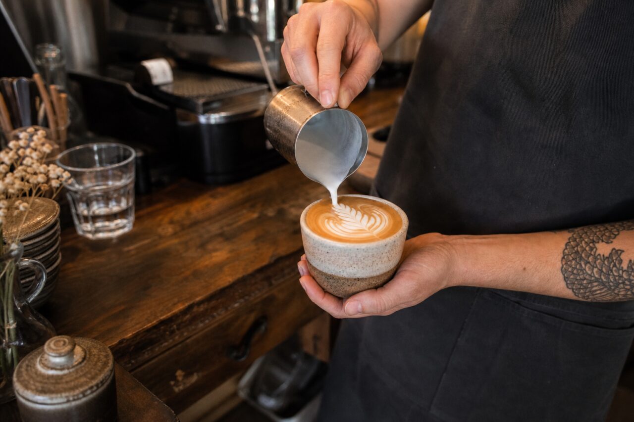 Personne dessinant un motif de feuille dans une tasse avec un pichet de lait