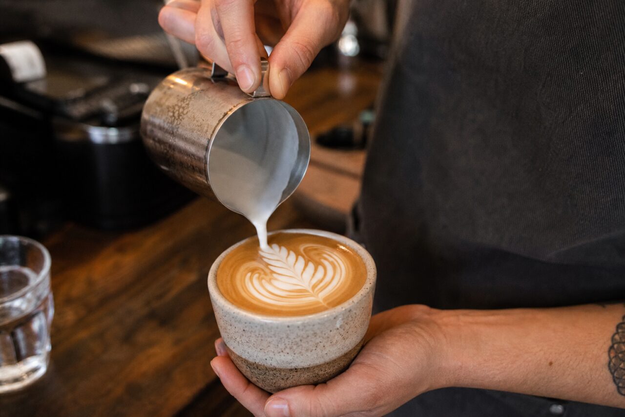 Persoon giet melk in een kop en maakt een bladpatroon op de koffie