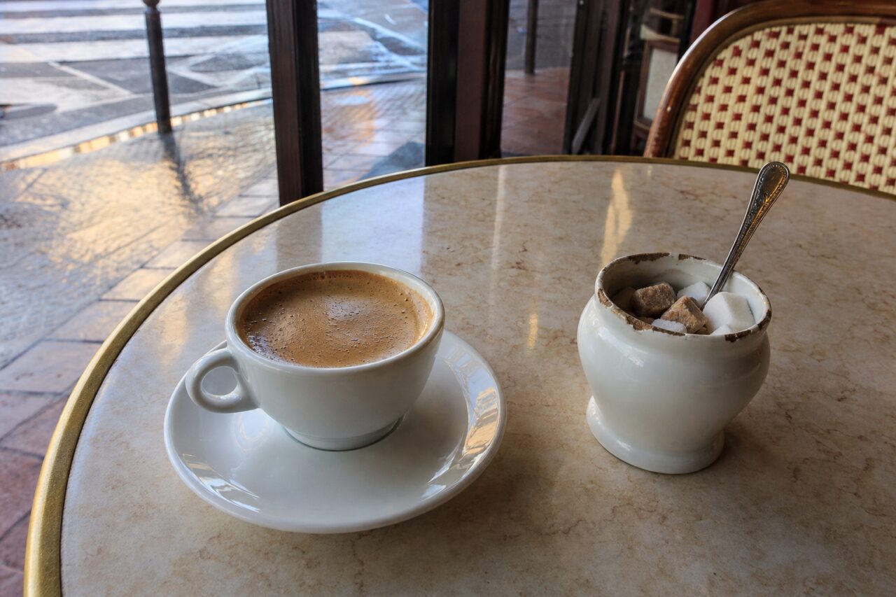 Kleiner Milchkaffee mit Zucker und Löffel auf einem Tisch an der Straße