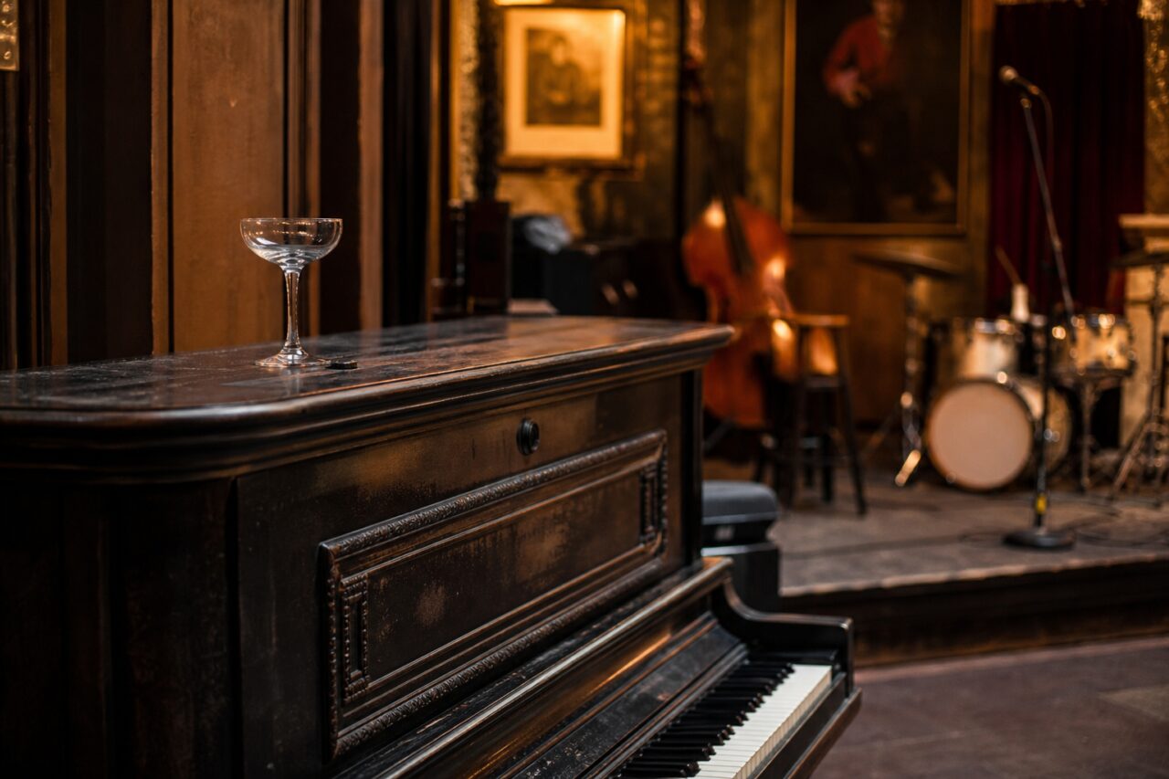 Black upright piano and cocktail glass in a bar with a jazz stage