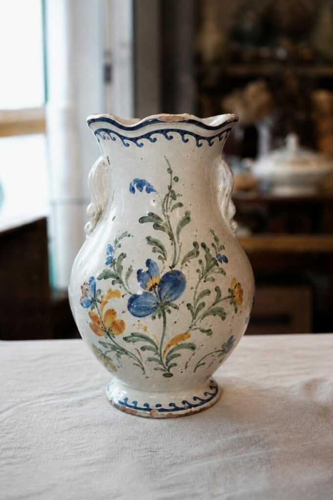 Portrait vertical de face d’un vase en faïence crème à bouquet bleu jaune et col ondulé