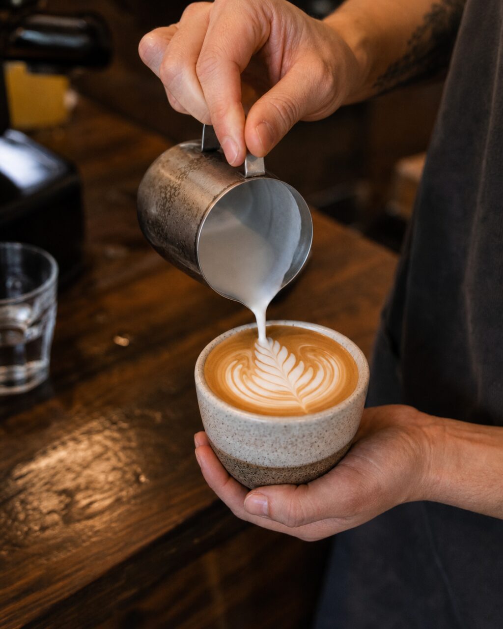 Milk pitcher pouring a leaf pattern into a cup in portrait view