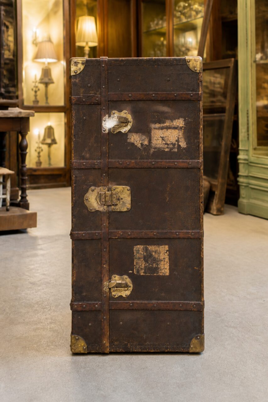 Portrait vertical d’une malle ancienne en cuir brun avec fermoirs superposés et coins métalliques