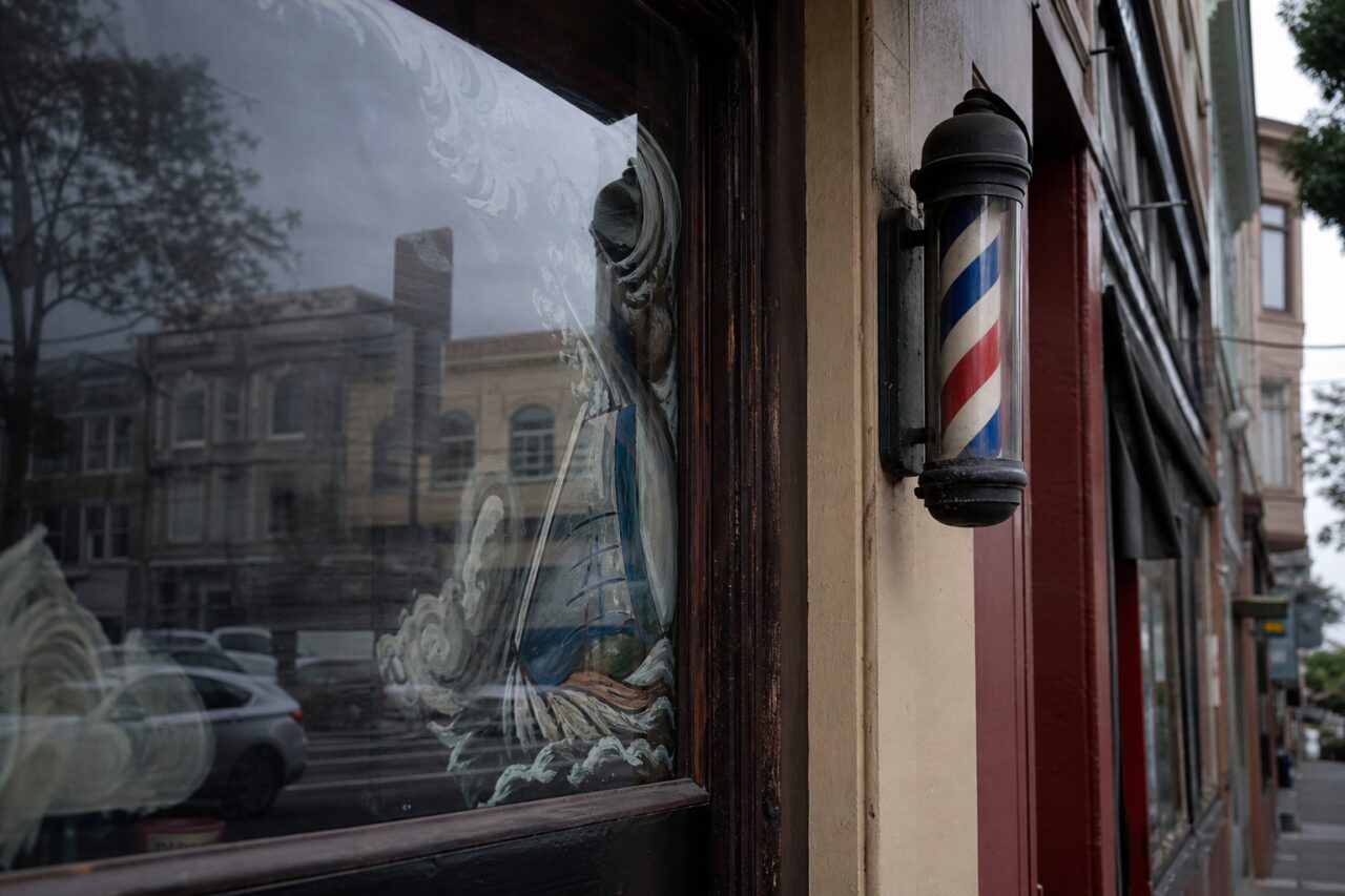 Poste de barbería tricolor junto a un escaparate decorado con reflejos de la calle