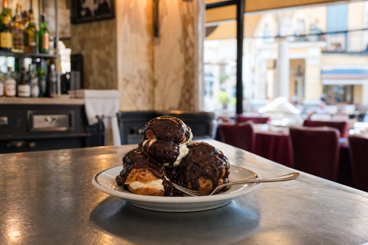 Profiteroles de chocolate servidas no centro de uma mesa de brasserie