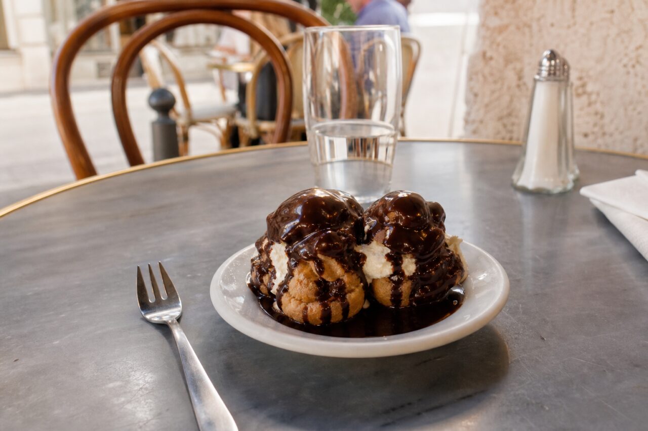 Profiterole al cioccolato con forchetta su un tavolo luminoso da brasserie
