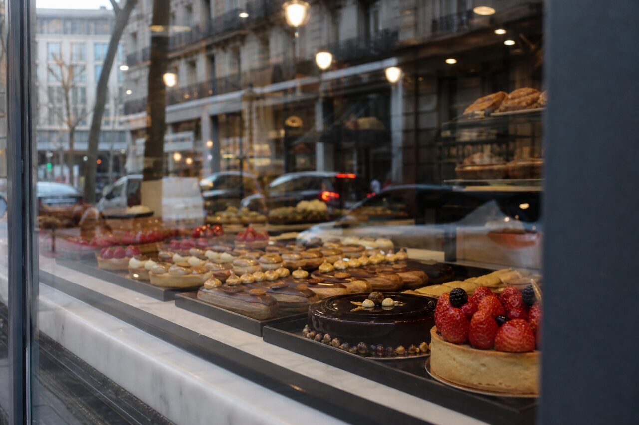 Straßenreflexionen über einer Vitrine mit Obsttorten und Schokoladenkuchen