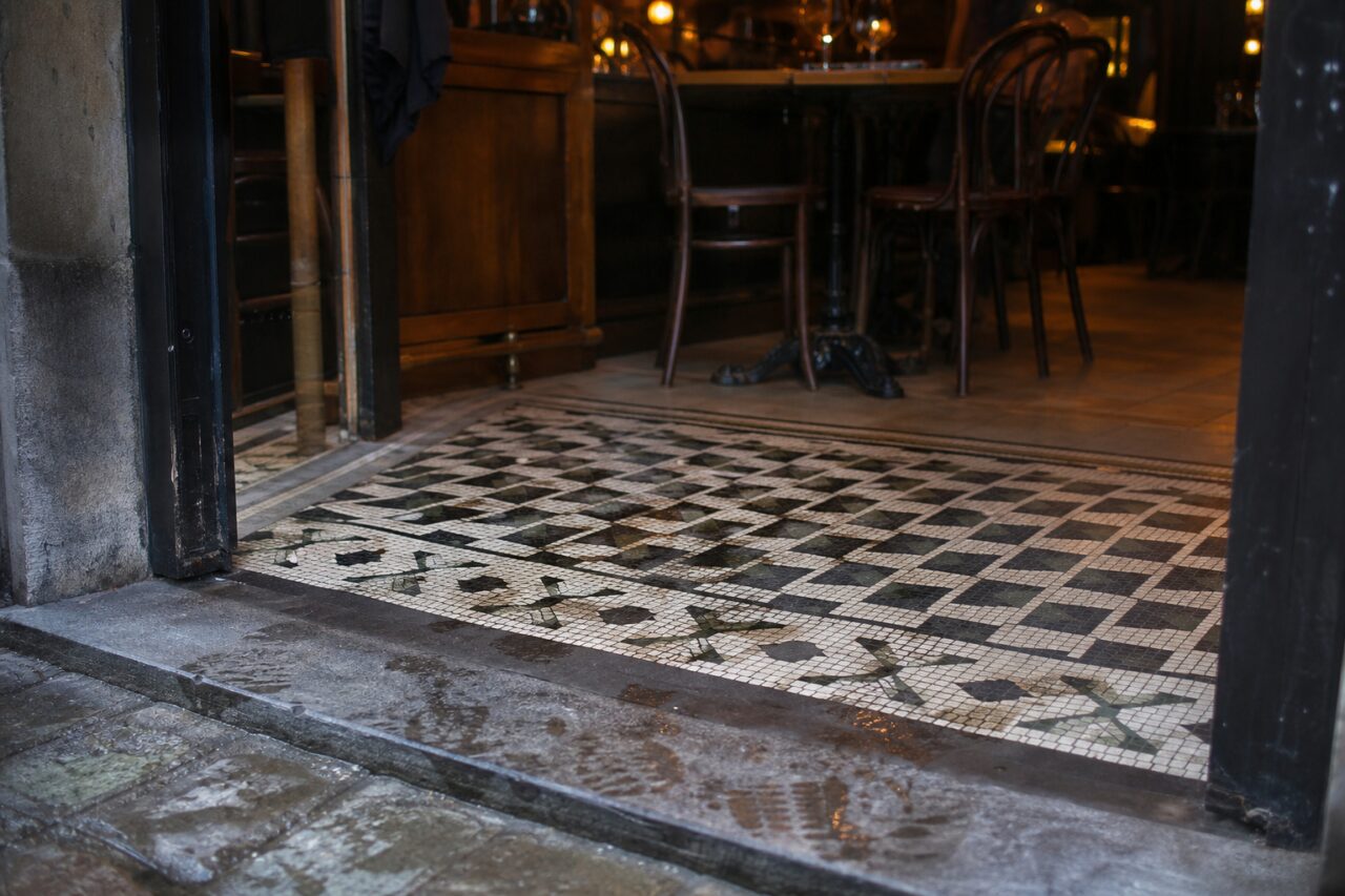 Black and cream mosaic floor at the threshold of a warmly lit brasserie