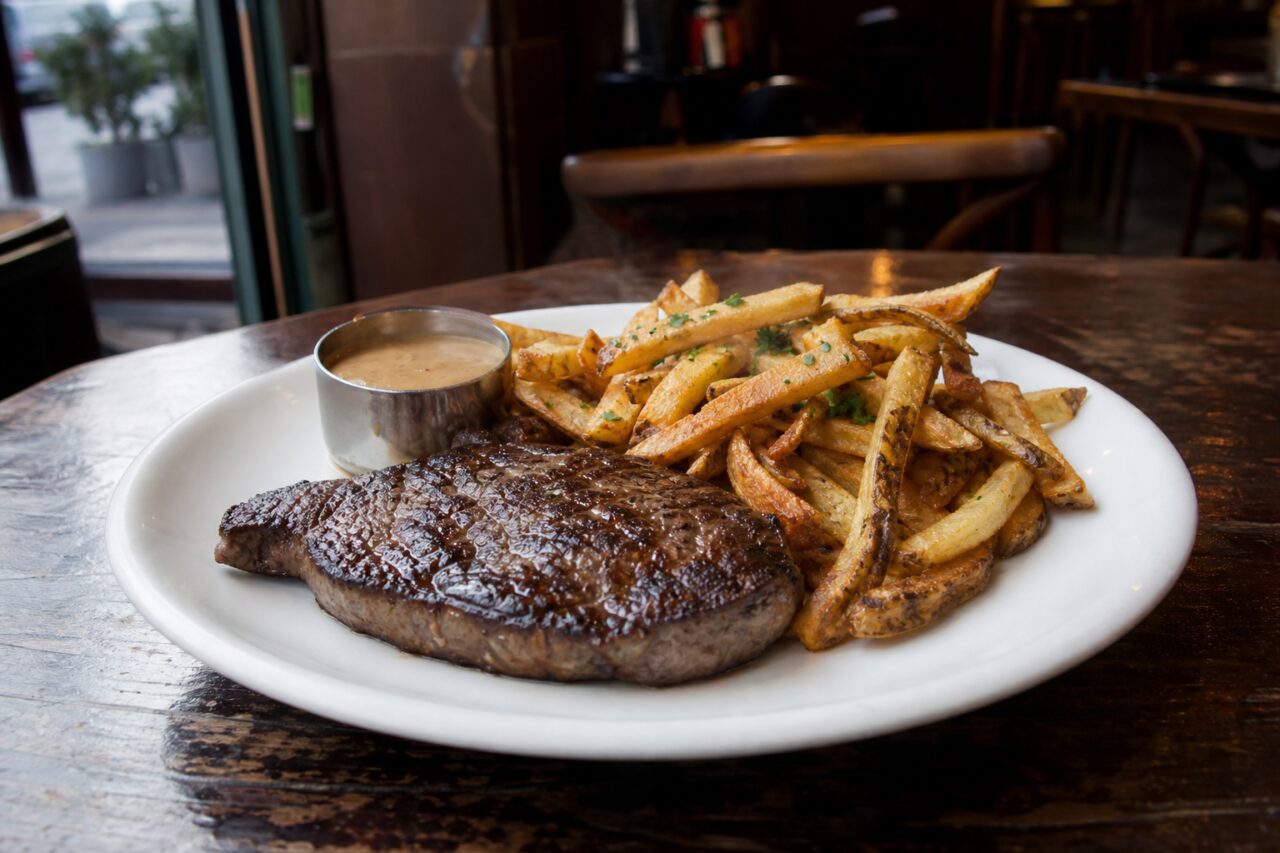 Gegrilde steak en goudbruine frieten met saus op een brasserietafel