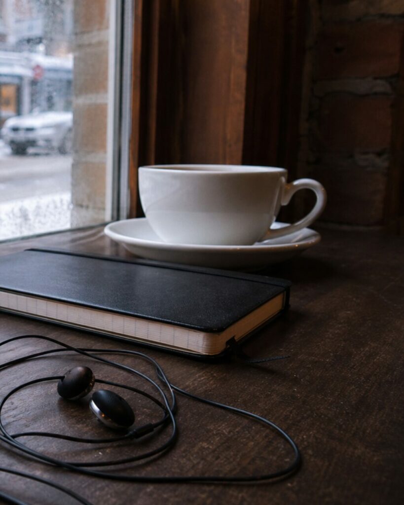 Tazza, taccuino e auricolari su un tavolo accanto al vetro