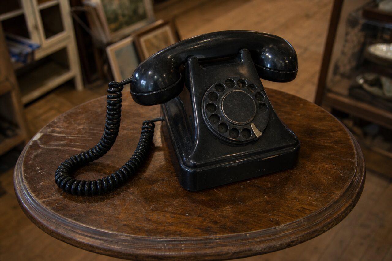 Altes Bakelittelefon in leichter Aufsicht mit Wählscheibe und Kabel auf einem runden Tisch