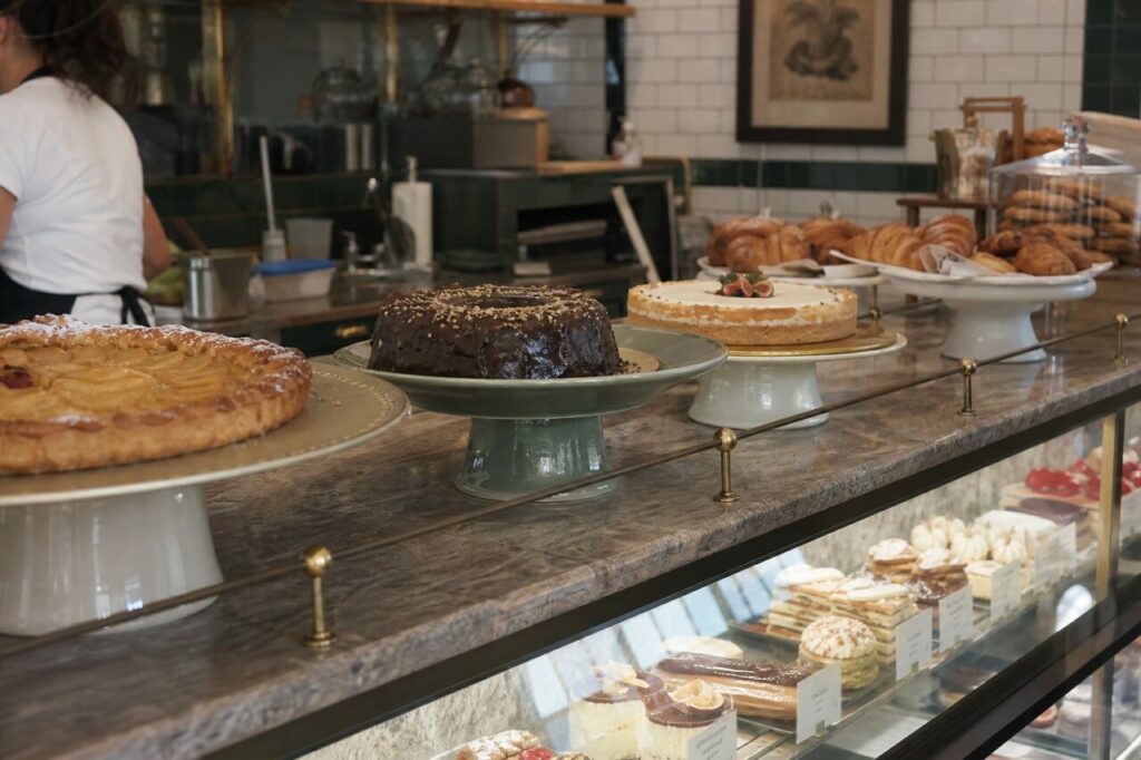 Trois gâteaux entiers sur présentoirs au-dessus d’une vitrine de desserts