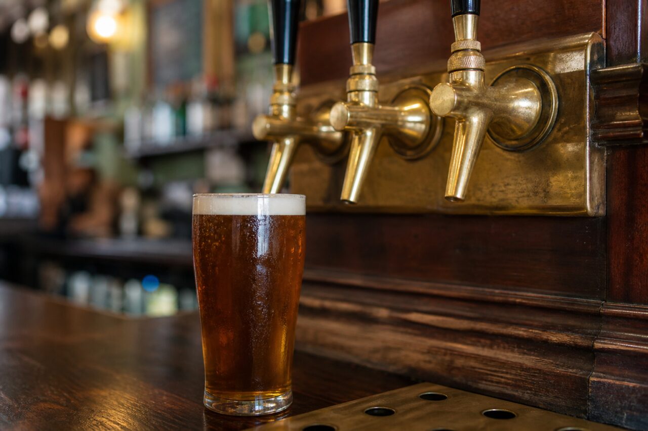 Drei Messingzapfhähne über einem Glas bernsteinfarbenem Bier