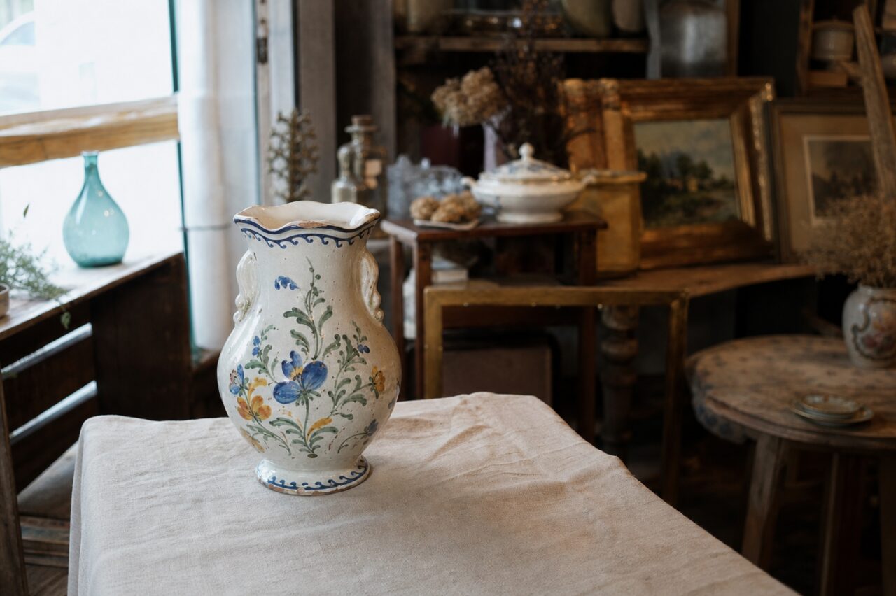 Vue large d’un vase en faïence fleuri parmi les meubles et objets d’une boutique d’antiquités