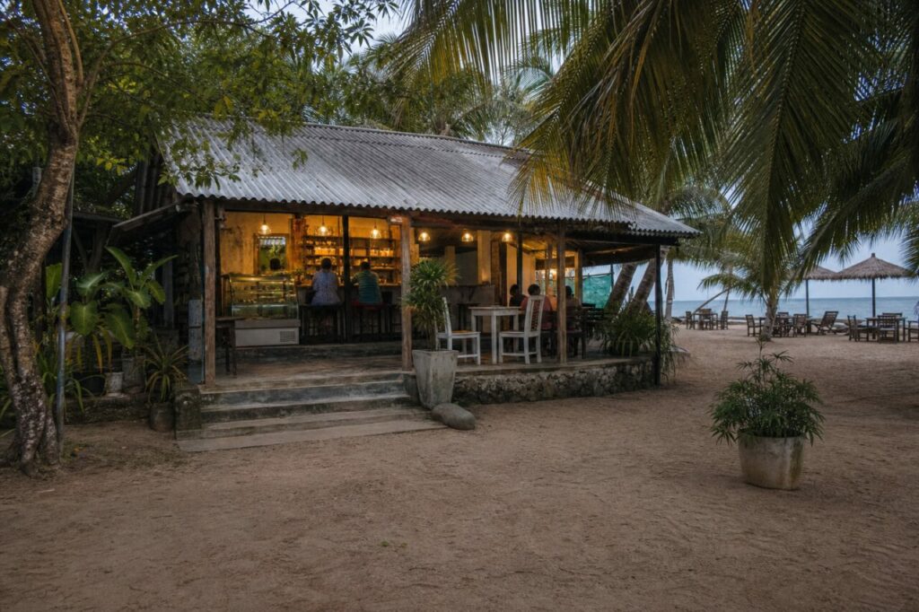 Vista amplia del café entre árboles y mesas de playa