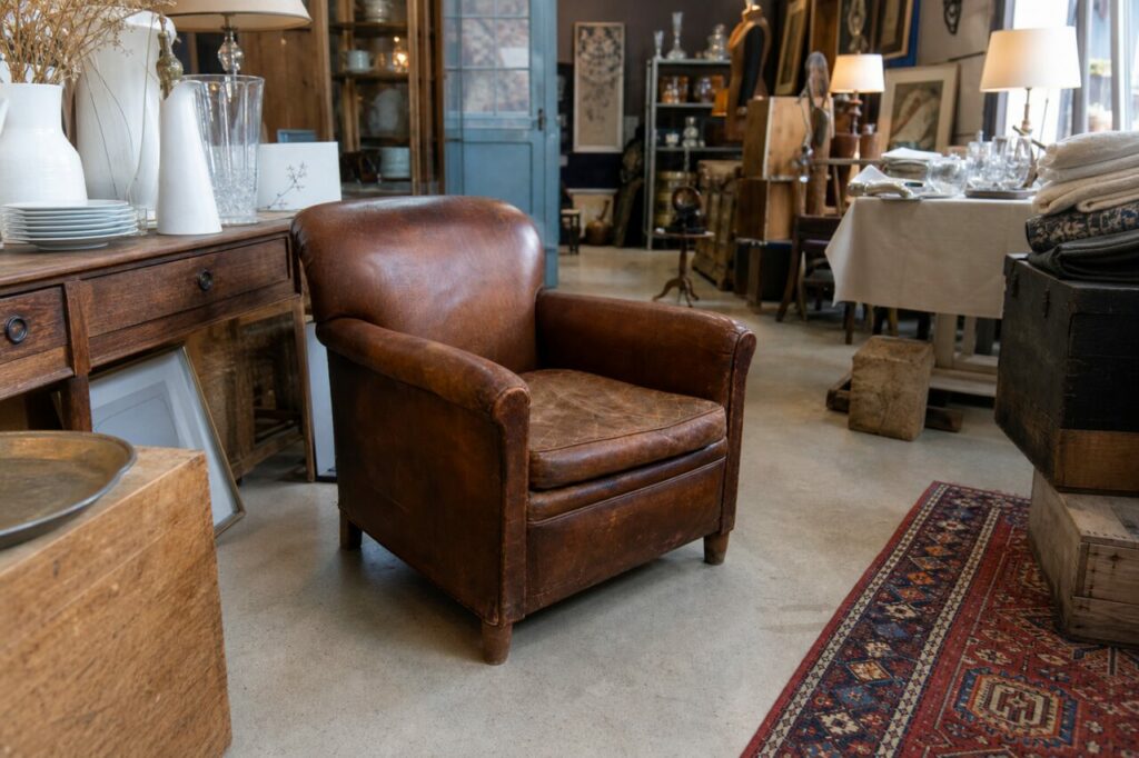 Vue large d’un fauteuil club en cuir brun au centre d’une boutique d’antiquités éclairée