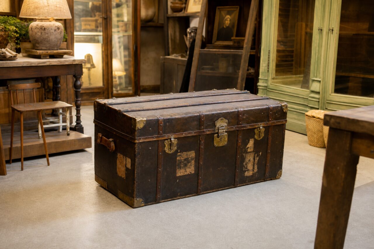 Wide interior view of a large brown leather trunk in an antiques shop with a green display cabinet