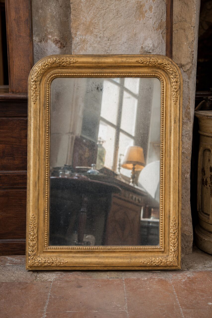 Front vertical view of a gilt Louis-Philippe-style mirror with marked glass and window reflection